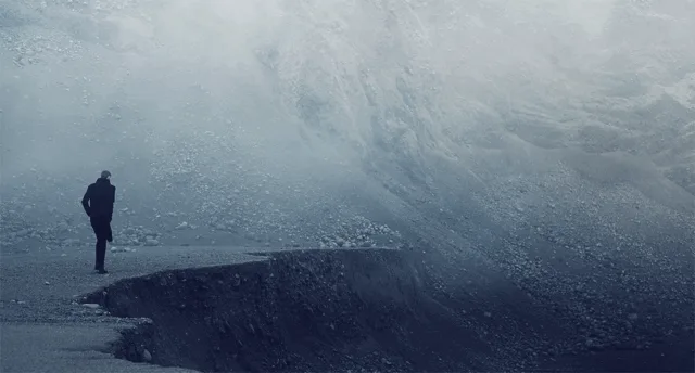 A lone figure standing where the road has collapsed into a mist-filled chasm — one step from the edge