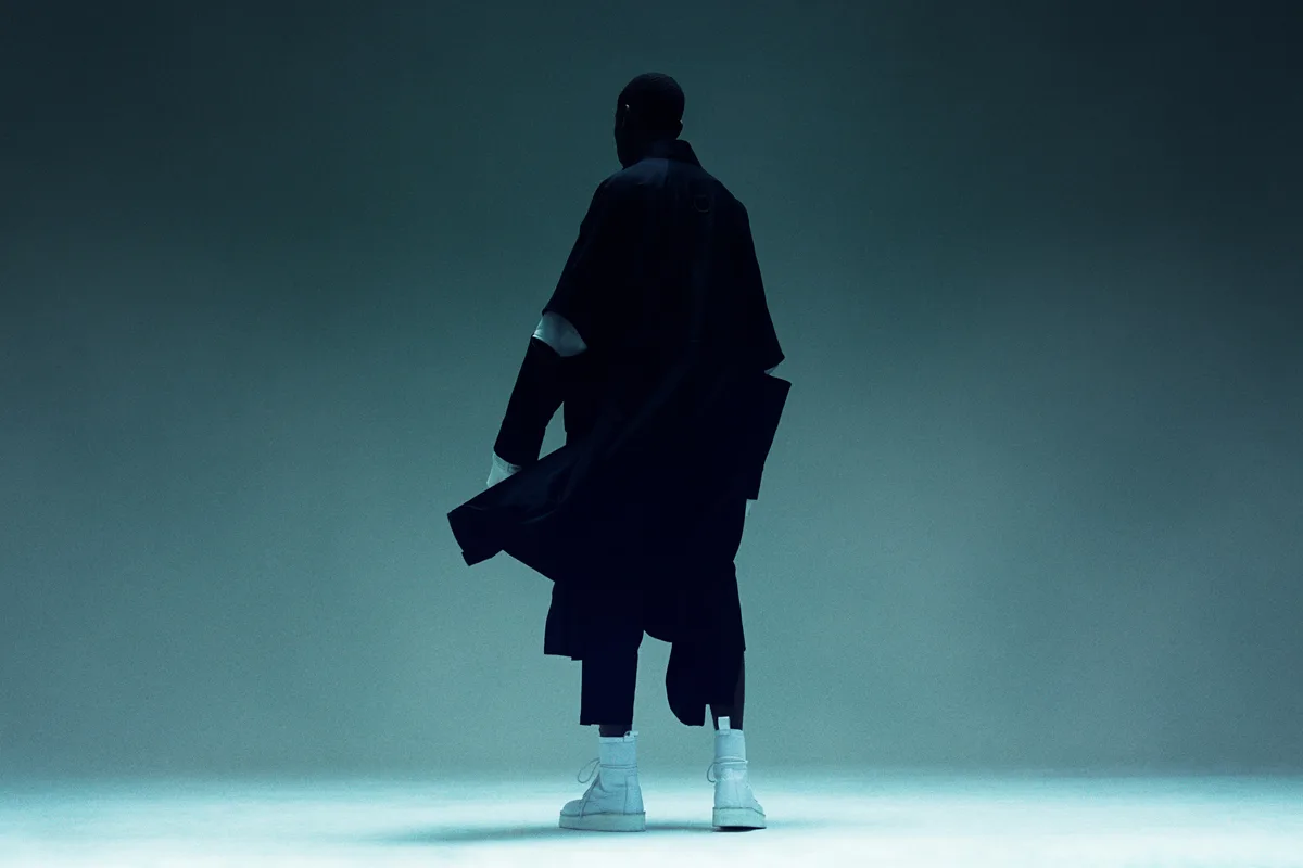 A cloaked silhouette standing in a teal-lit void